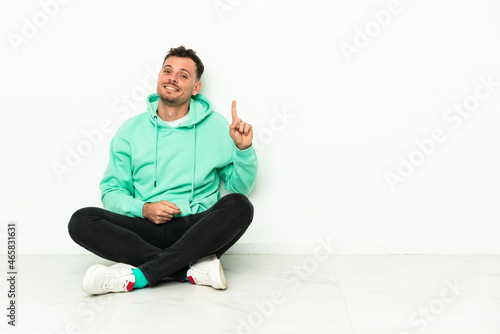 Young handsome caucasian man sitting on the floor pointing with the index finger a great idea