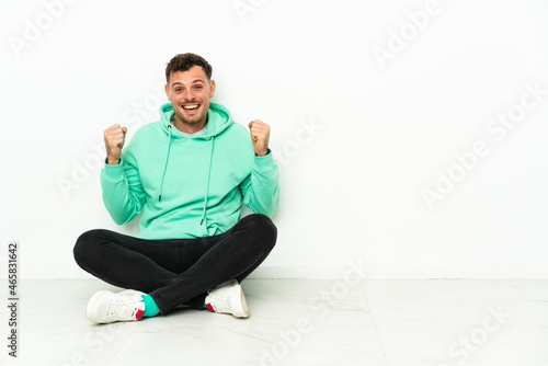 Young handsome caucasian man sitting on the floor celebrating a victory in winner position © luismolinero