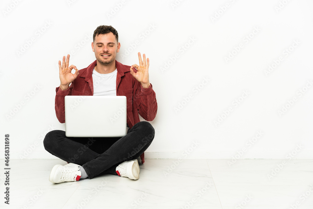 Young handsome caucasian man sit-in on the floor with laptop in zen pose Young handsome caucasian man sit-in on the floor with laptop in zen pose