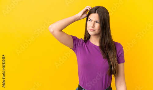Teenager Brazilian girl over isolated yellow background having doubts while scratching head