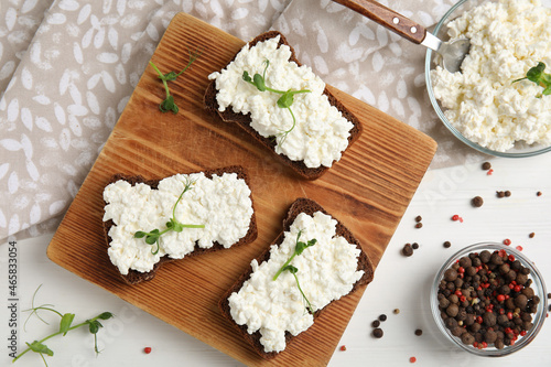 Bread with cottage cheese and microgreens on white wooden table, flat lay