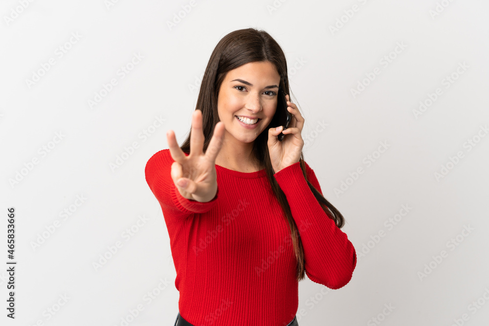 Teenager Brazilian girl using mobile phone over isolated white background happy and counting three with fingers