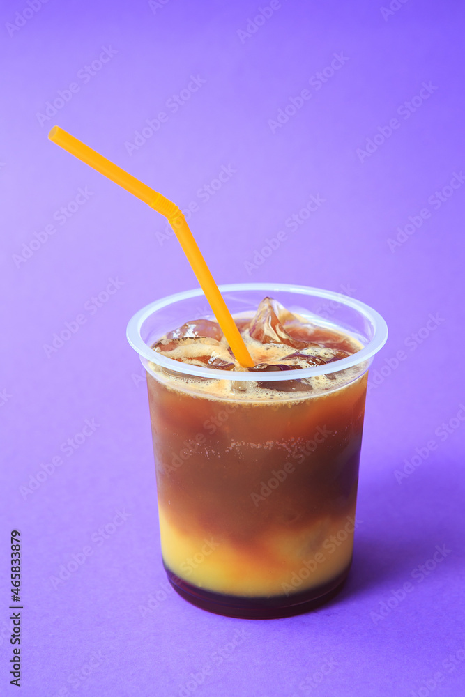 A glass with orange coffee cocktail cold refreshing drink or beverage with ice on violet background A glass with orange coffee cocktail cold refreshing drink or beverage with ice on violet background