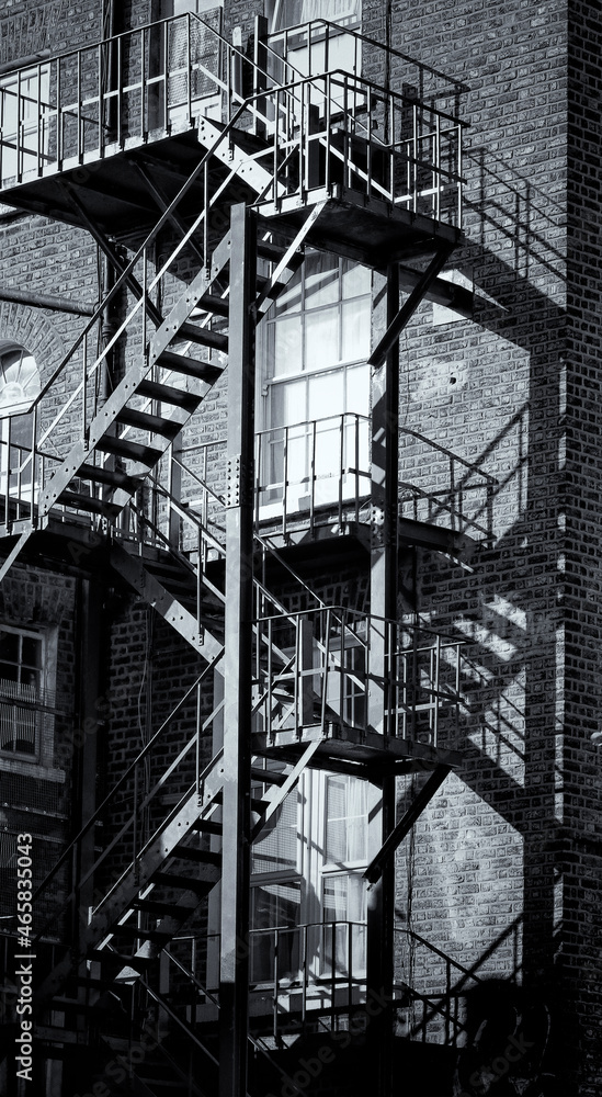 Obraz premium Linear shadows cast by sunlight on exterior metal fire escape of old building. Street in Dublin, Ireland. Deliberate grainy texture effect in monochrome black and white