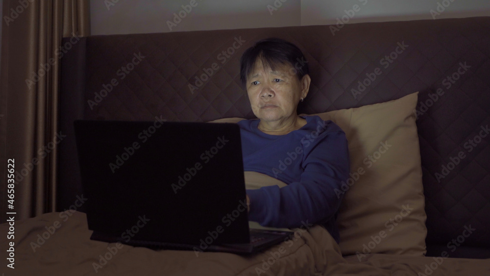 Depressed elderly old Asian woman, people using a notebook laptop computer on social media internet on bed in bedroom at home. Lifestyle on late night in technology device concept. Insomnia Depressed elderly old Asian woman, people using a notebook laptop computer on social media internet on bed in bedroom at home. Lifestyle on late night in technology device concept. Insomnia