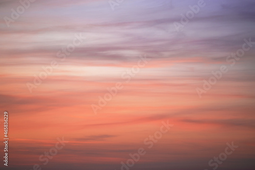 The sky at sunset with feather clouds. The color of the sky changes from purple to dark orange.