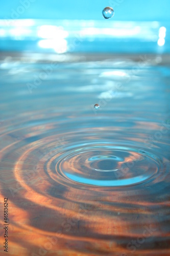 Movimiento de agua en ondas por goteo formando burbujas en el aire sobre el agua de la cubeta de vidrio con fondo azul.