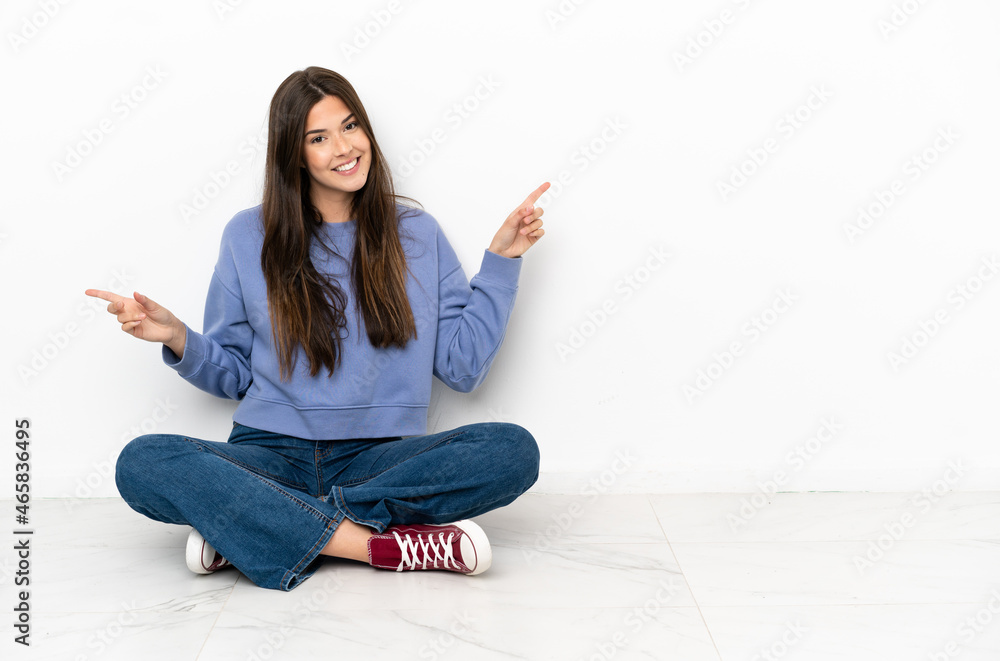 Young woman sitting on the floor pointing finger to the laterals and happy Young woman sitting on the floor pointing finger to the laterals and happy