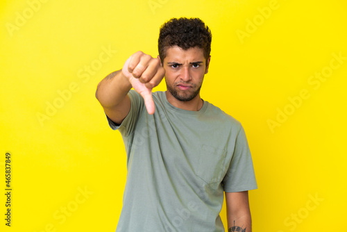 Young handsome Brazilian man isolated on yellow background showing thumb down with negative expression