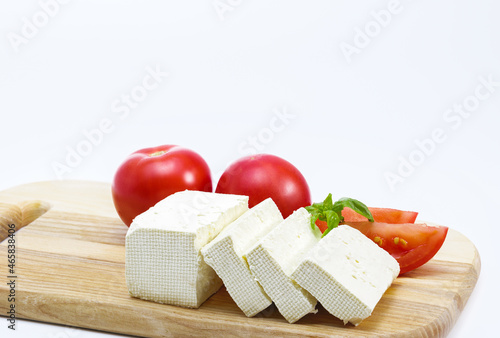 Feta cheese, ripe tomatoes, tomato slices, basil on a wooden board