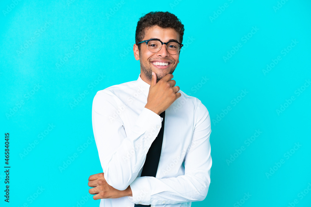Young business Brazilian man isolated on blue background with glasses and smiling Young business Brazilian man isolated on blue background with glasses and smiling