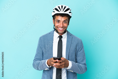 Young business Brazilian man with bike helmet isolated on blue background sending a message with the mobile © luismolinero