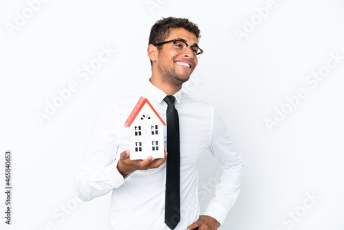 Young business Brazilian man holding a house toy isolated on white background posing with arms at hip and smiling