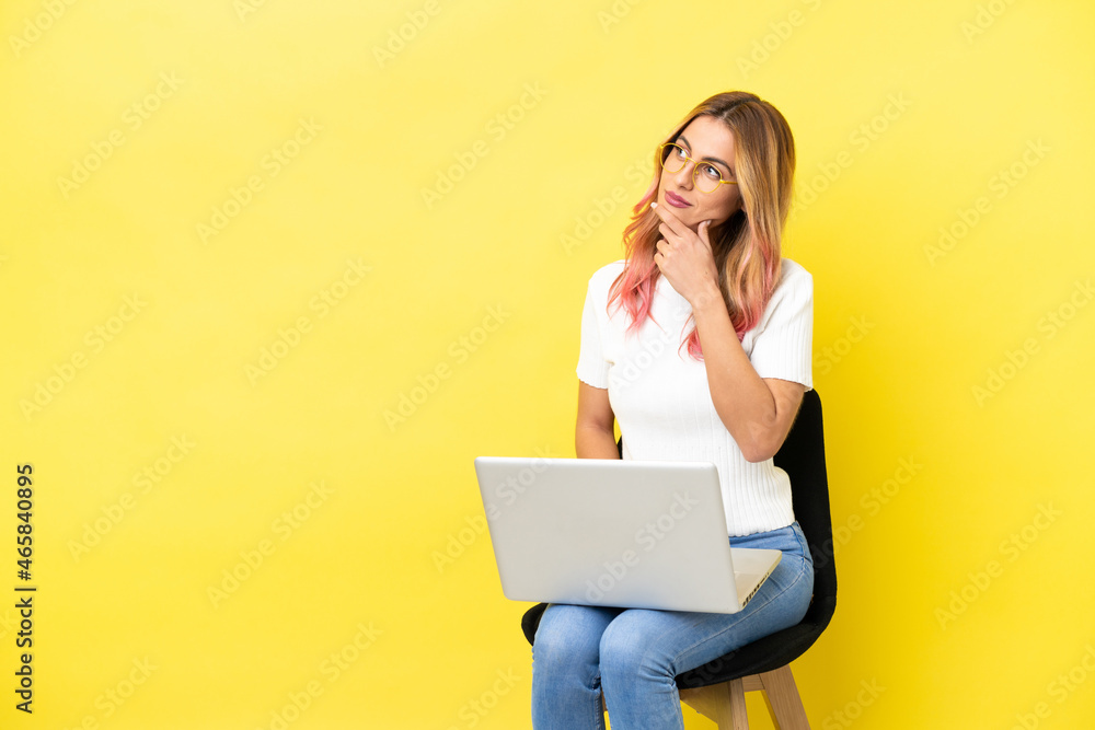 Naklejka premium Young woman sitting on a chair with laptop over isolated yellow background having doubts
