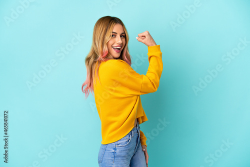 Young woman over isolated blue background doing strong gesture © luismolinero