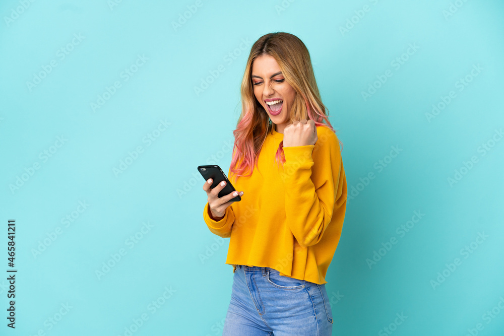 Young woman over isolated blue background with phone in victory position Young woman over isolated blue background with phone in victory position