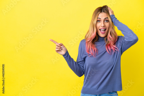 Young woman over isolated yellow background surprised and pointing finger to the side