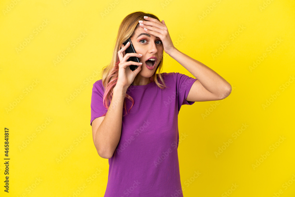 Young woman using mobile phone over isolated yellow background doing surprise gesture while looking to the side Young woman using mobile phone over isolated yellow background doing surprise gesture while looking to the side