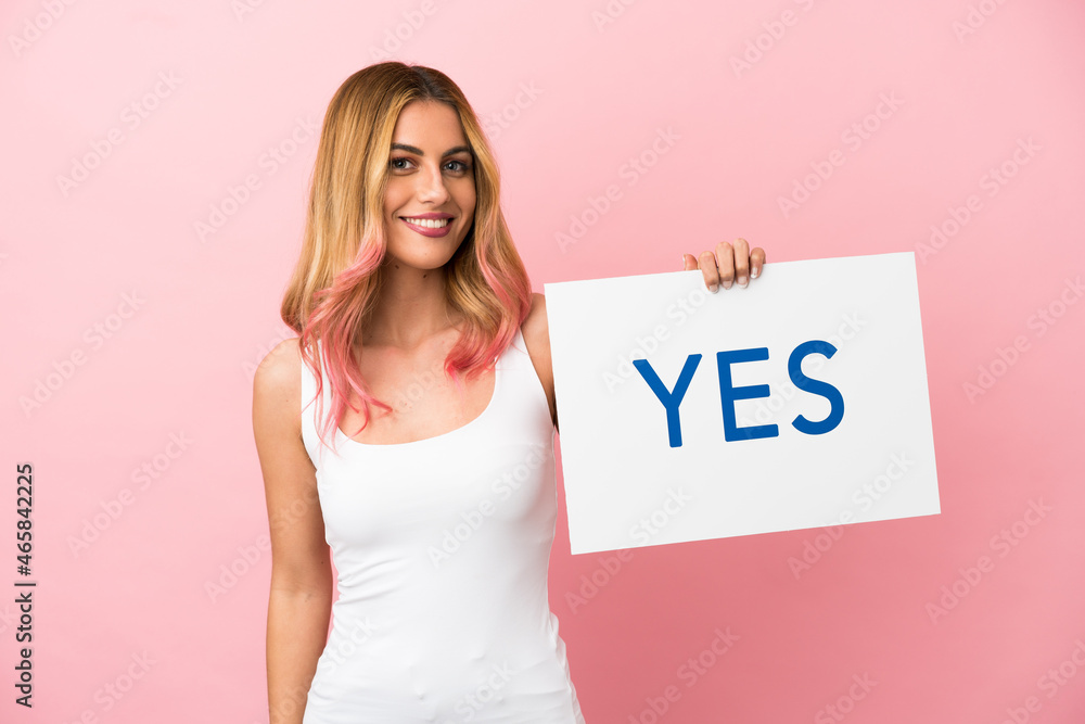 Young woman over isolated pink background holding a placard with text YES with happy expression Young woman over isolated pink background holding a placard with text YES with happy expression