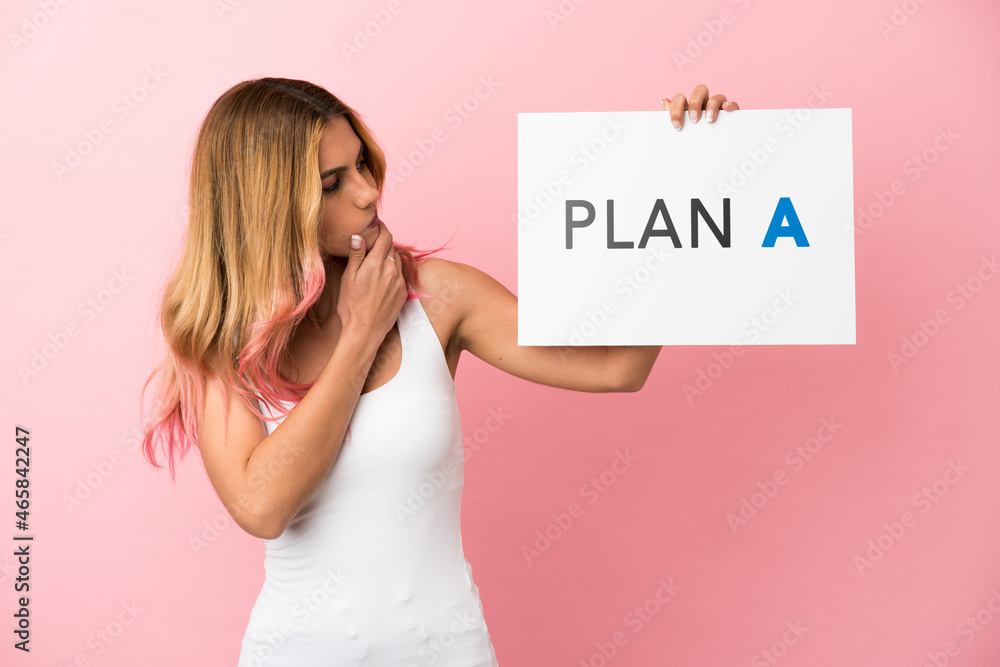 Young woman over isolated pink background holding a placard with the message PLAN A and thinking Young woman over isolated pink background holding a placard with the message PLAN A and thinking