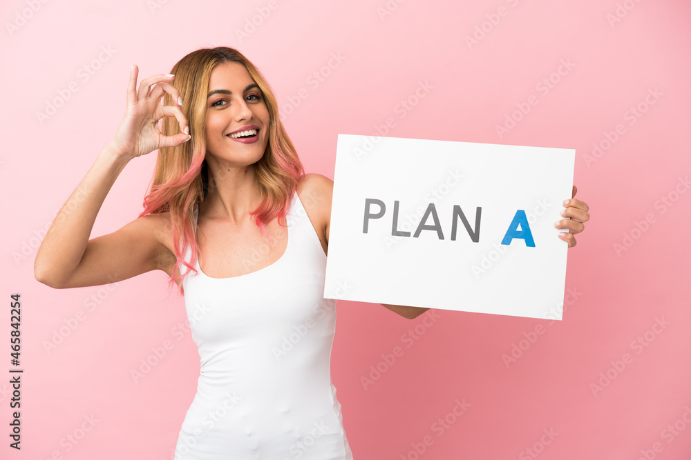 Young woman over isolated pink background holding a placard with the message PLAN A with ok sign Young woman over isolated pink background holding a placard with the message PLAN A with ok sign