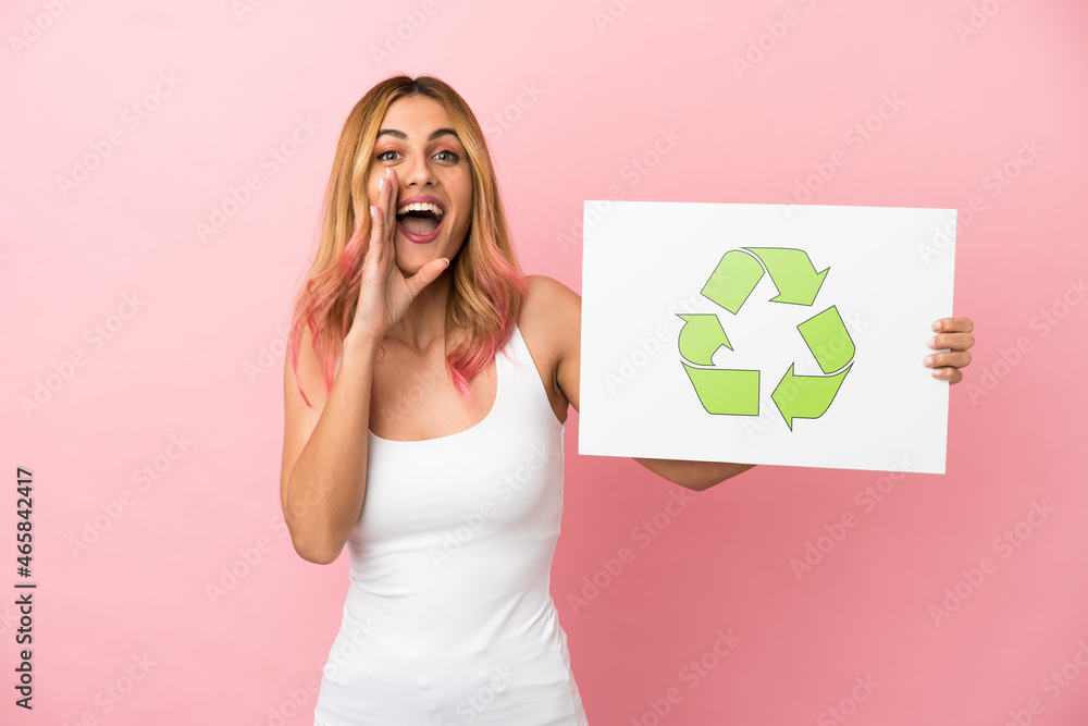 Young woman over isolated pink background holding a placard with recycle icon and shouting