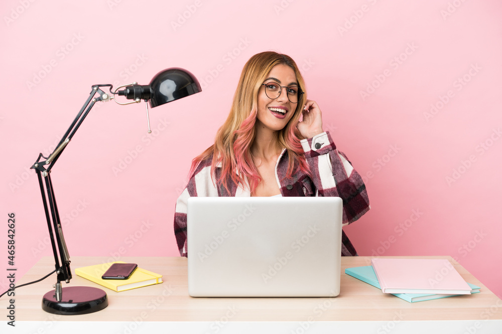Young student woman in a workplace with a laptop over pink background laughing Young student woman in a workplace with a laptop over pink background laughing