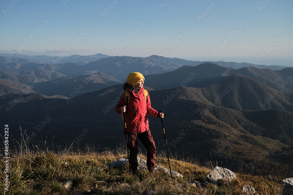 Travel in autumn and enjoy beautiful panoramic view. Female traveler in red jacket and with yellow backpack is engaged in hiking and trekking in Caucasus mountains. Explore new places alone.