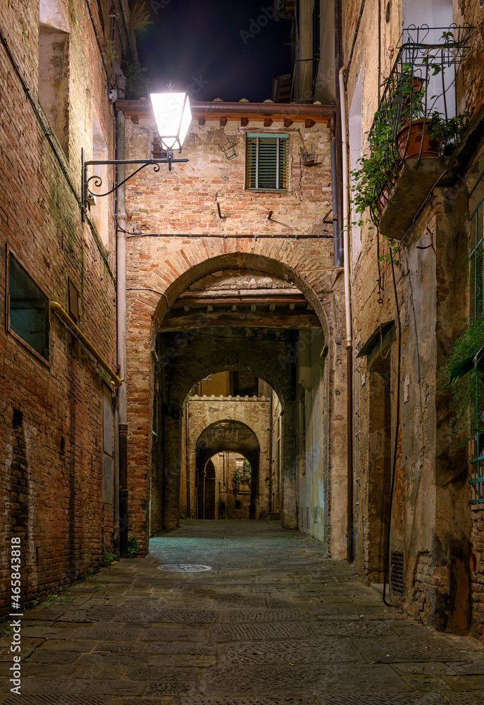 Medieval narrow street in Siena at night, Tuscany, Italy. Architecture and landmark of Siena. Cozy cityscape of Siena