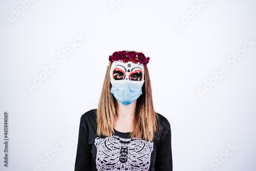 woman wearing mexican face mask during halloween celebration. skeleton costume and red roses diadem on head. woman wearing blue face mask during pandemic corona virus. Halloween party concept