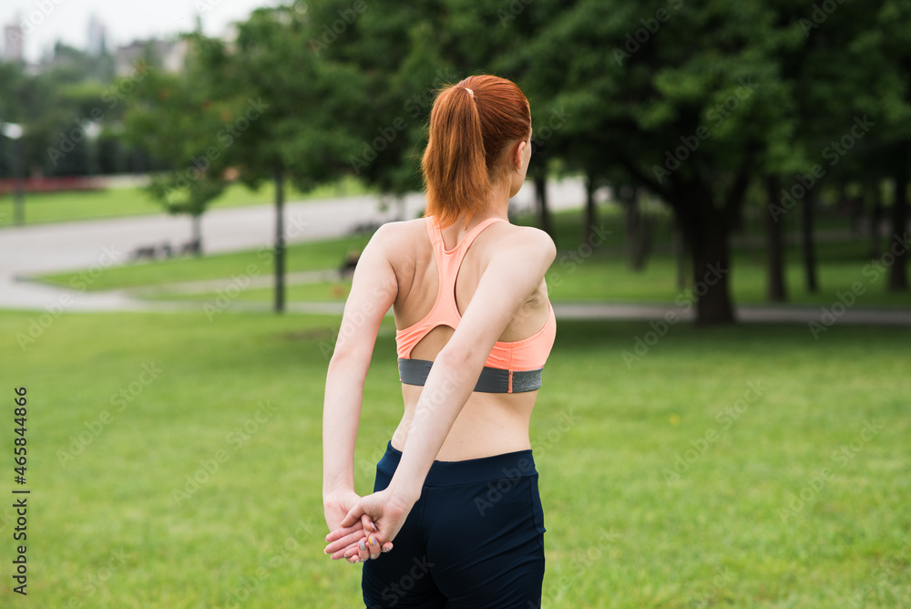 Redhead woman stretching in the park on the grass Redhead woman stretching in the park on the grass