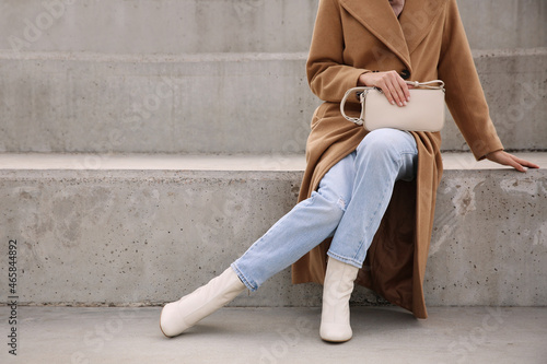 Stylish woman with trendy beige bag on stairs outdoors, closeup photo