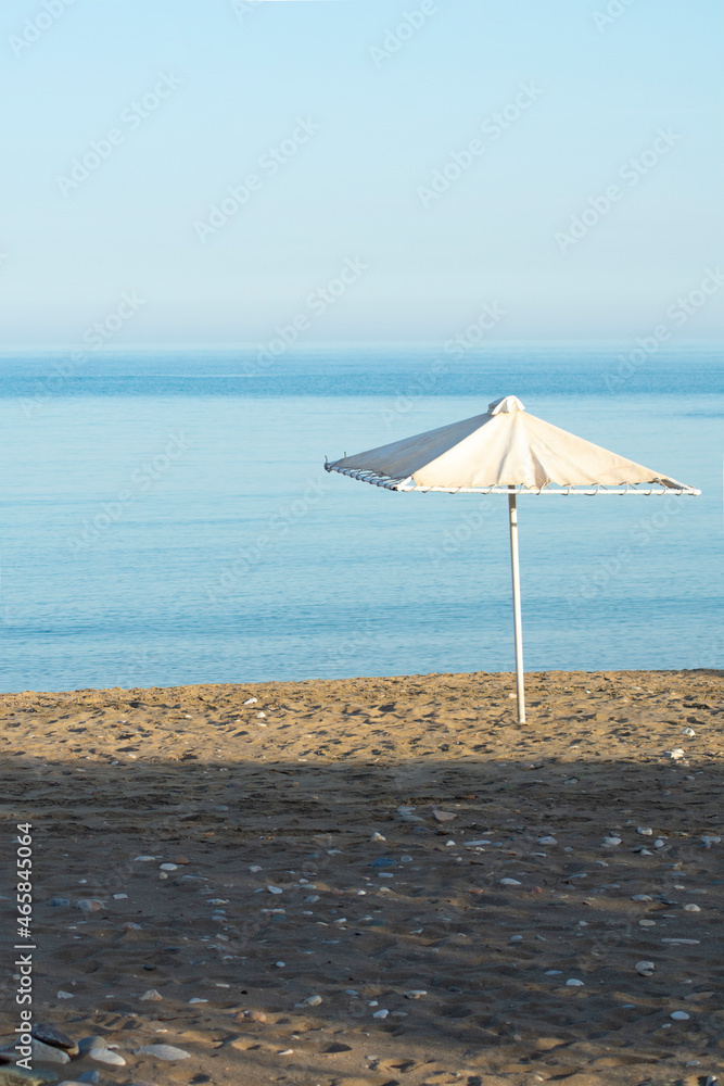 Lone parasol on a sandy beach at secluded Sikinos island, Greece. Vertical shot with copy space. Lone parasol on a sandy beach at secluded Sikinos island, Greece. Vertical shot with copy space.