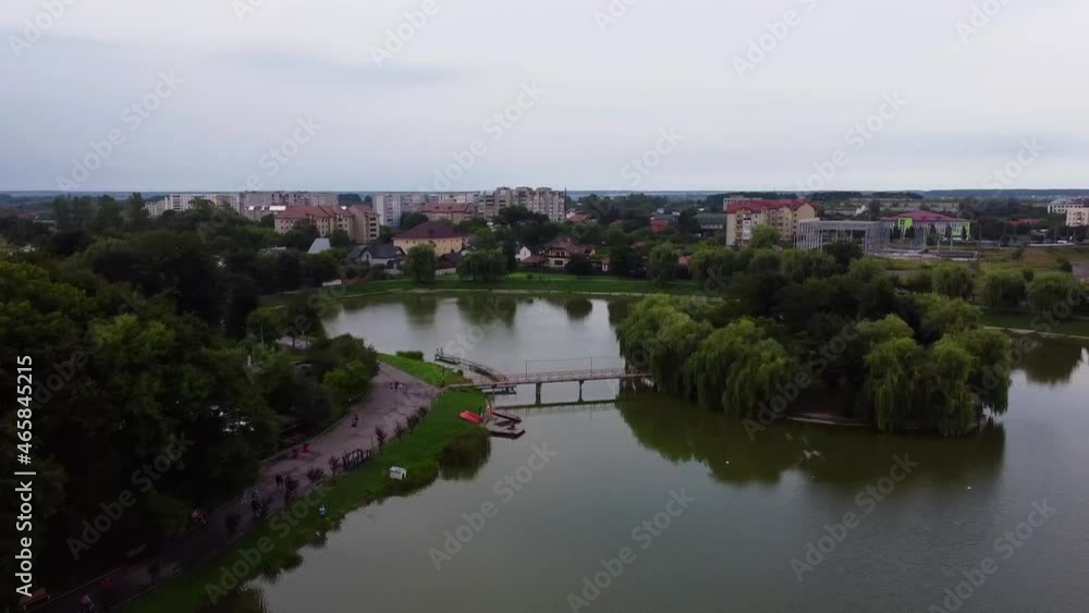 View of the artificial island in the pond in Kolomiya. Houses near the lake in the city park. Bridge in the water. Drone Video. Ukraine. Europe View of the artificial island in the pond in Kolomiya. Houses near the lake in the city park. Bridge in the water. Drone Video. Ukraine. Europe