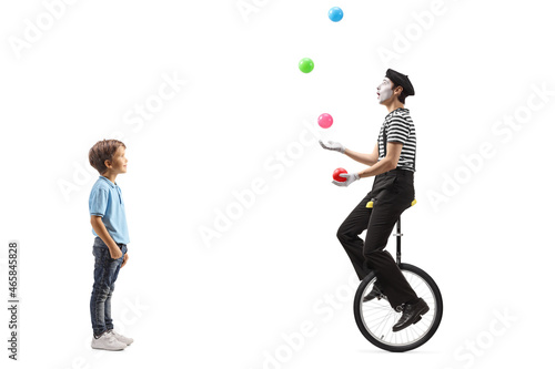 Full length profile shot of a little boy looking at a mime juggling with balls and riding a unicycle photo
