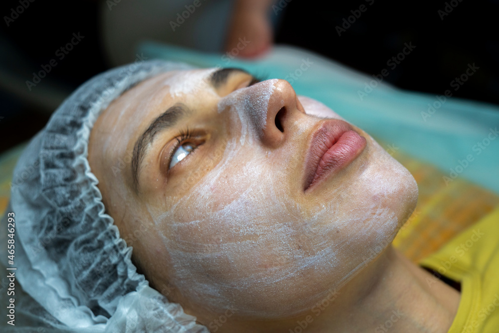 Beauty clinic concept. Young woman getting professional facial procedure. Beautician spreads mask on female face with brush. Face renovation concept. Lateral view. Beauty clinic concept. Young woman getting professional facial procedure. Beautician spreads mask on female face with brush. Face renovation concept. Lateral view.