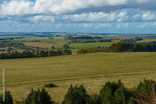 long English countryside view of green fields, woodlands and a big blue and white cloud sky seen from Sidbury Hill, Wiltshire UK