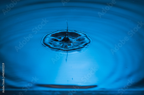 Close up view of drops making circles on blue water surface isolated on background.