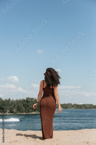 A young sexy woman barefoot and in a summer dress walks along the edge of the river