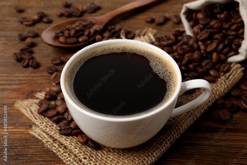 Cup of aromatic hot coffee and beans on wooden table