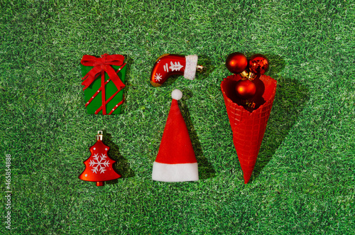 A bright infographic with Christmas decoration: a Christmas tree, a gift, a boot, Santa's hat and a red ice cream cone with red balls, on artificial grass. New Year in nature background design