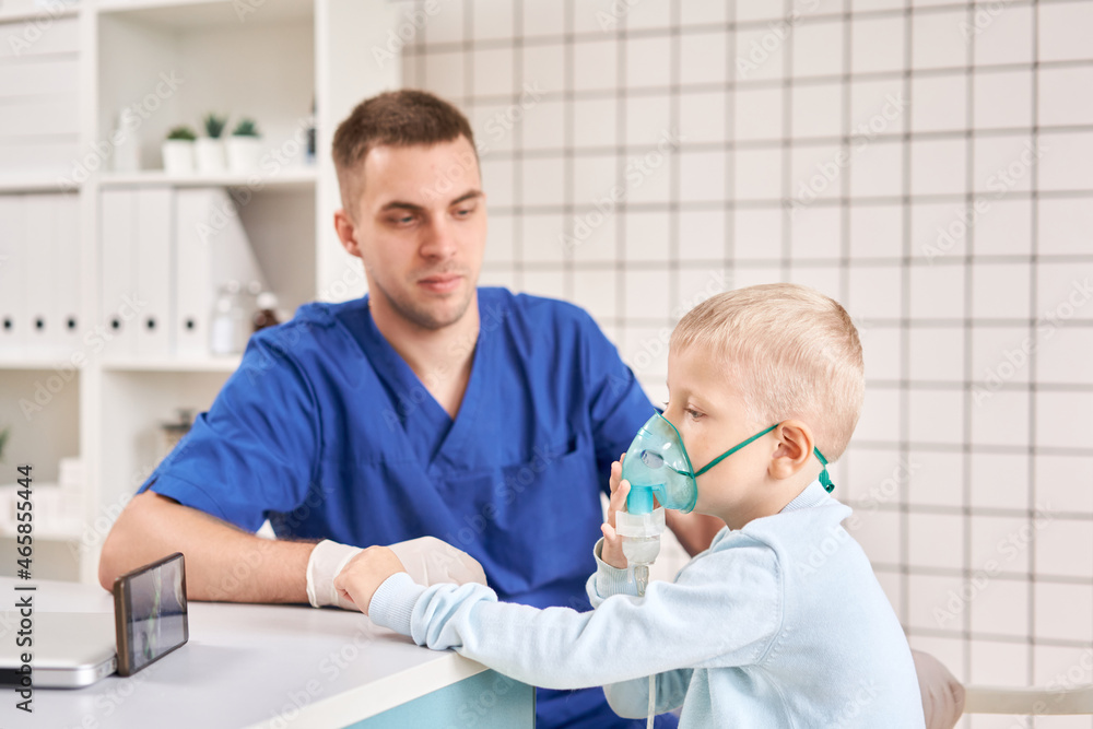 Fototapeta premium A pediatrician diagnoses lung disease and provides treatment. Breathe the medicine through a nebulizer inhaler.. Portrait of adorable little boy visiting doctor.