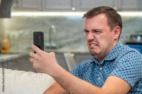 Fotografia Annoyed millennial man with disgust look at smartphone screen at modern living room
