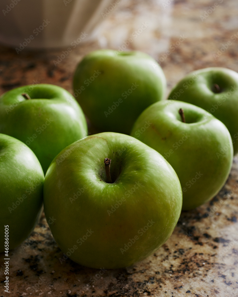 Granny Smith apples whole on granite countertop with large bowl in background. Granny Smith apples whole on granite countertop with large bowl in background.