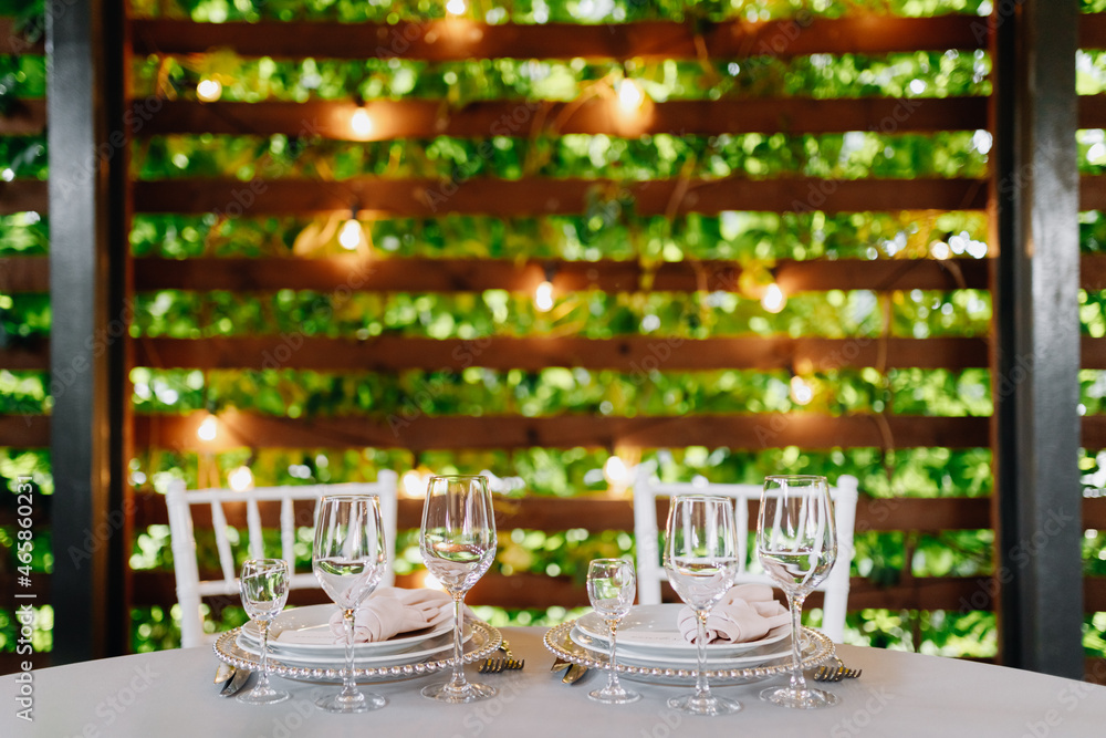 Glasses, plates, white chairs close-up on a background of lights. Place for your text