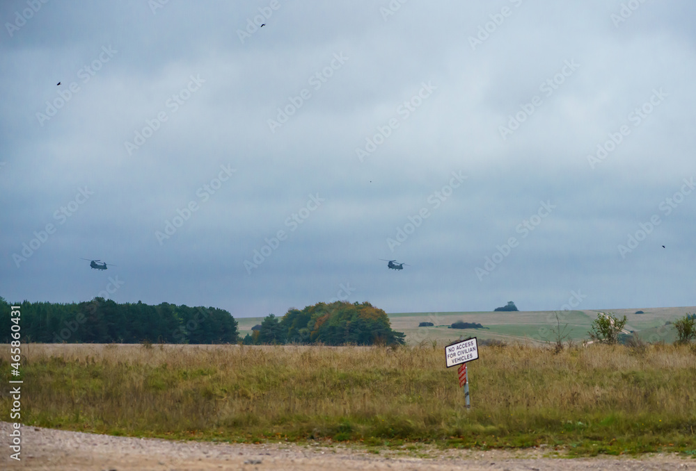 Two British Army Boeing CH-47 Chinook helicopters flying low in a cloudy blue grey and white winter sky on a military exercise, Wiltshire UK