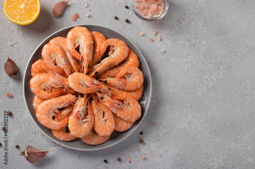 Boiled shrimps in a round plate and spices on a light gray background. Space for text