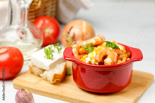 Greek appetizer, Saganaki. Shrimp baked with vegetables and cheese, a portion in a red pot. Close-up, selective focus