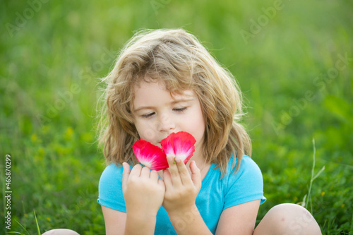 Close up portrait of a small blond boy smelling flowers. Kids enjoying summer.
