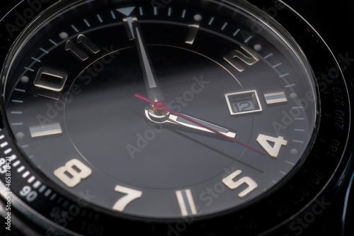 macro shot of a black wrist watch marking 4:00. silver details and red pointer